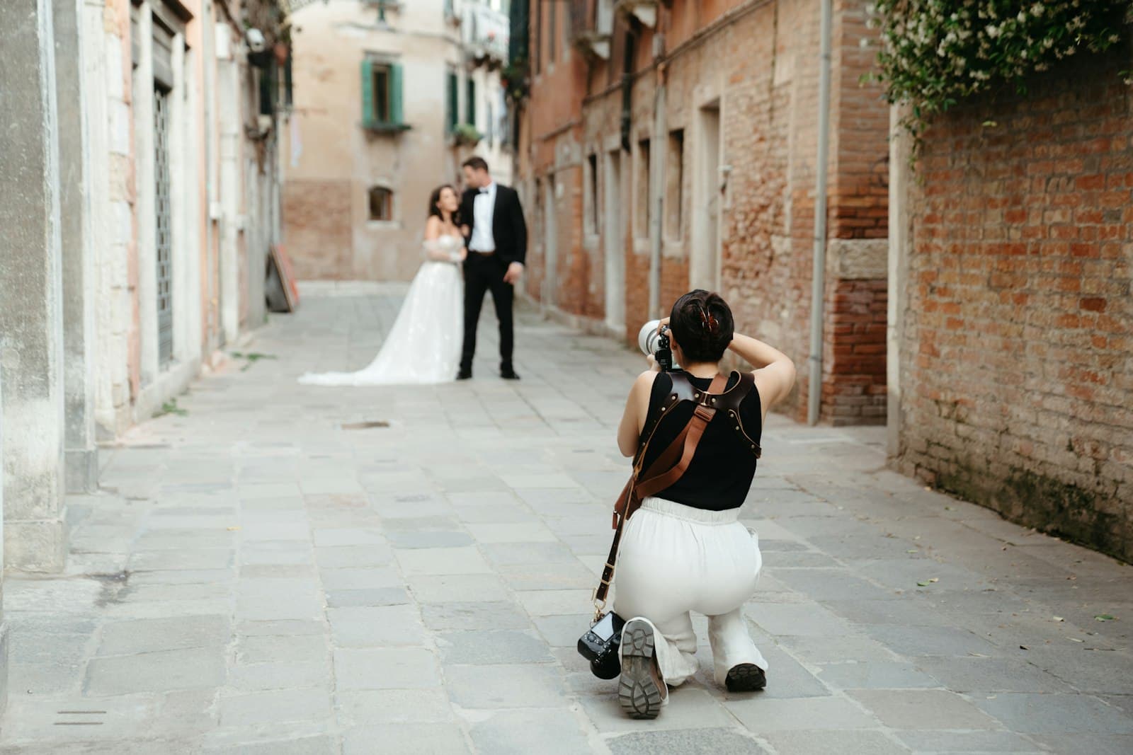 A photographer kneeling in a Venice alley to photograph a couple in wedding attire